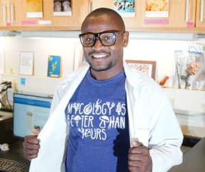 African american mycology student with purple t-shirt that says Mycology Is Better Than Yours