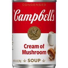 A can of Campbell’s Condensed Cream of Mushroom Soup with the iconic red and white label, gold medallion seal, and an image of sliced mushrooms on the lower right corner.
