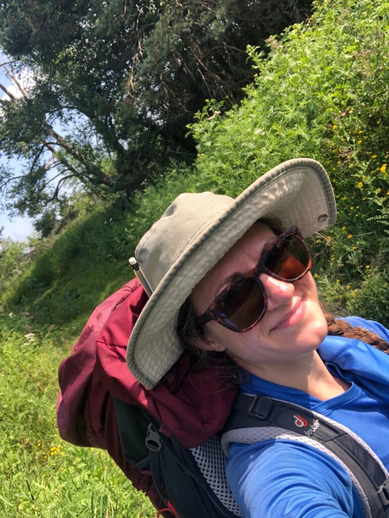 Shannon Meehan wearing a tan hat, blue shirt, sunglasses, and a red backpack.