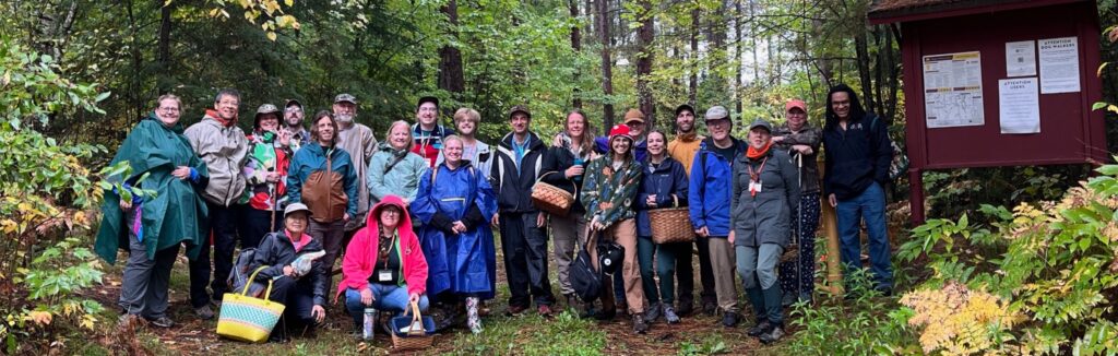 Group photo of 2025 Cloquet Forestry Center Weekend participants in the woods with foray baskets and rain gear.