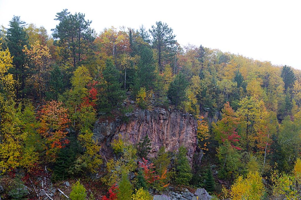 Red and gray cliffs surrounded by colorful fall foliage on the edge of a mine pit in Lake Vermilion State Park, MN