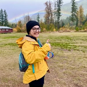 Oliver Filialuna standing in a clearing in a mountainous area wearing a yellow rain jacket and blue backpack.